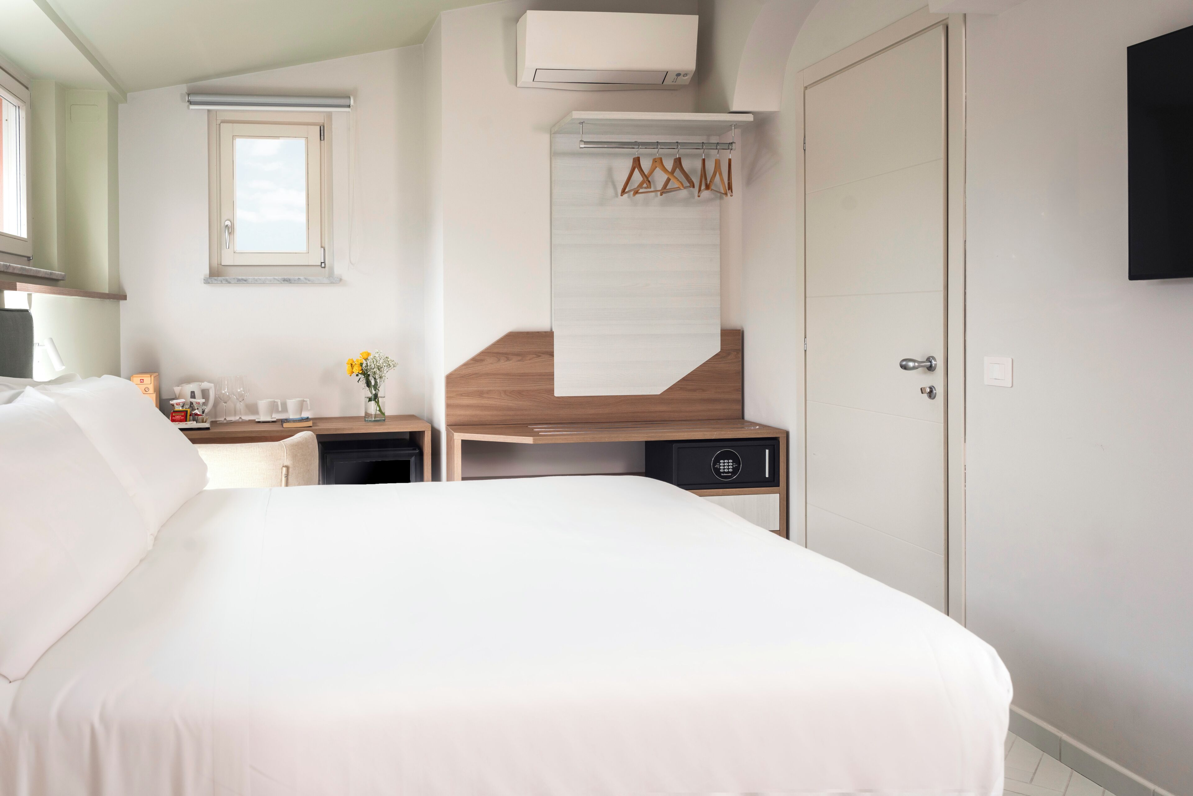 Habitación de hotel con cama, escritorio, armario, ventana y televisor montado.