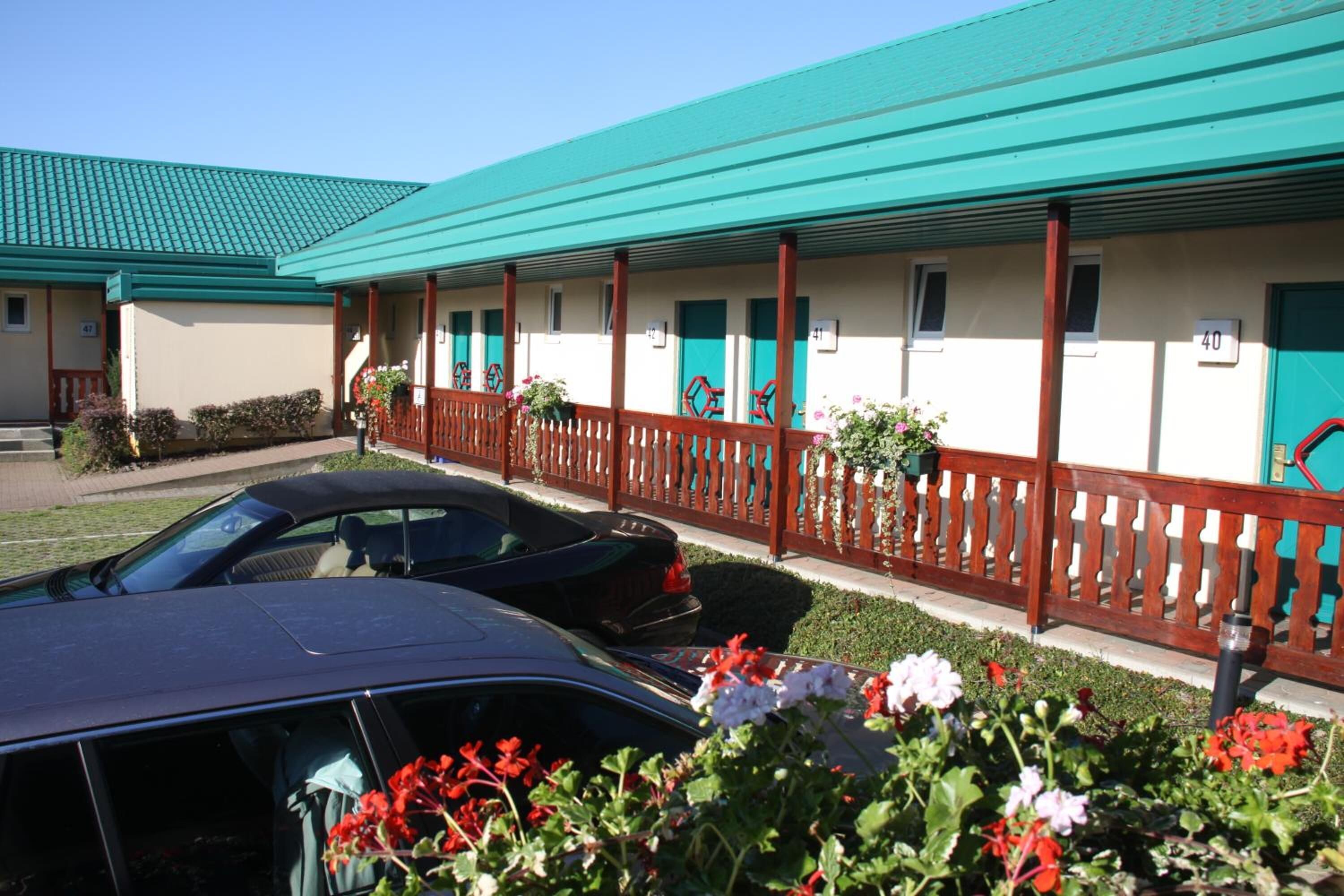 Motelzimmer in einer Reihe mit türkisblauen Dächern und Holzgeländern.