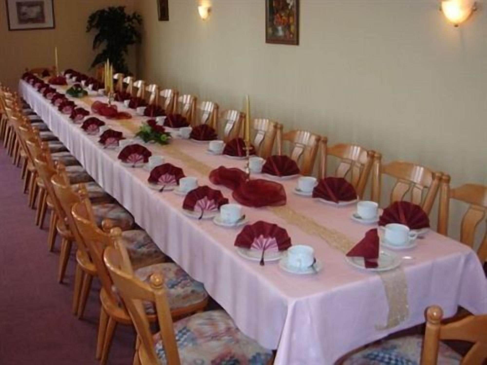 Een lange eettafel gedekt met witte borden, rode servetten en gouden kandelaars.