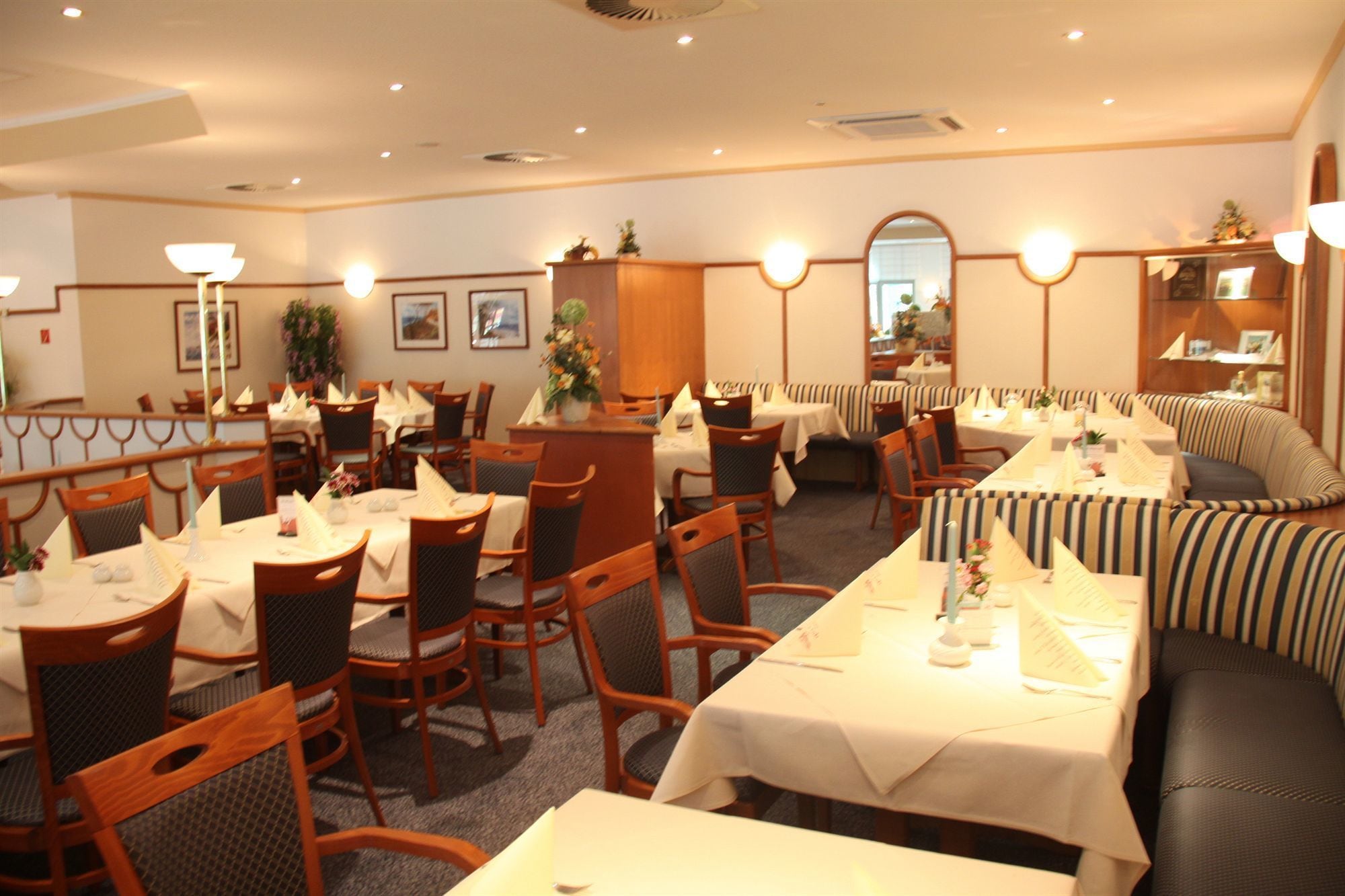 Een restaurant met meerdere tafels en zitjes, houten stoelen en een gestreepte bank.