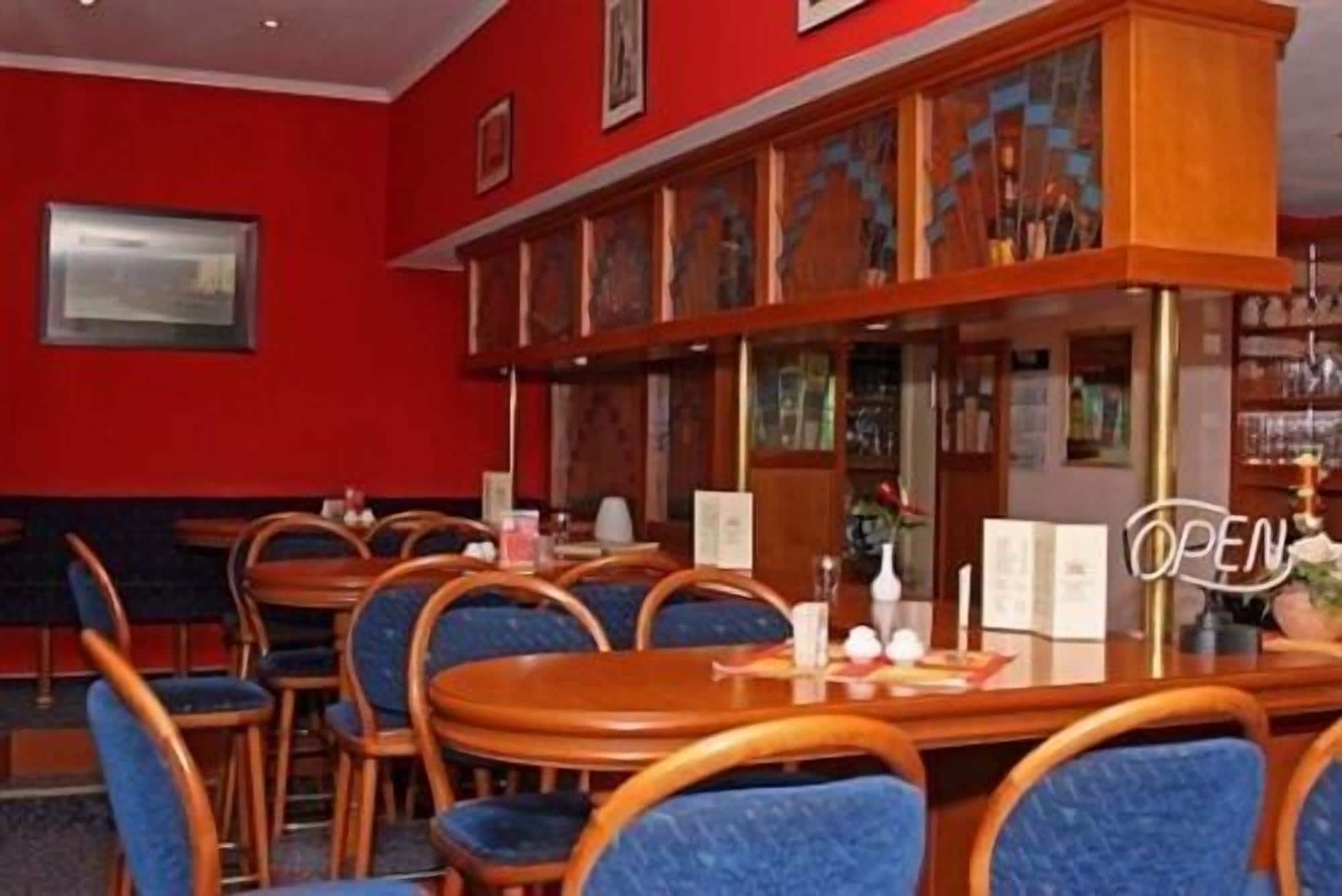 A restaurant with wooden tables and blue chairs, a red wall, and a 'OPEN' sign.