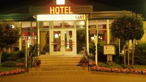 Entrada de hotel con recepción y restaurante, escalones que conducen a la entrada, y un cartel que indica un mercado cercano.