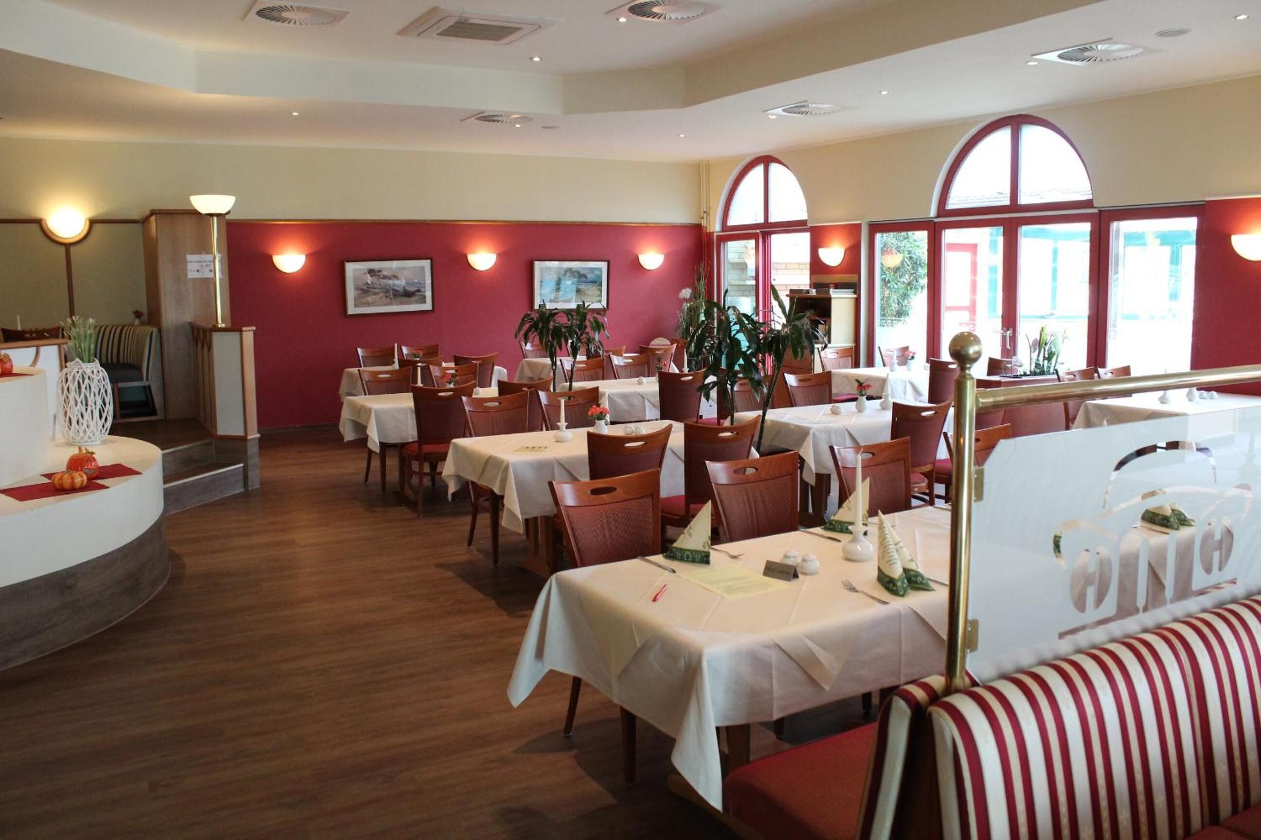 A restaurant with multiple tables and chairs, red walls, and large windows.