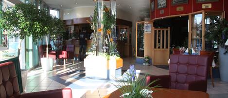 A hotel lobby with a reception desk, seating area, and large windows.
