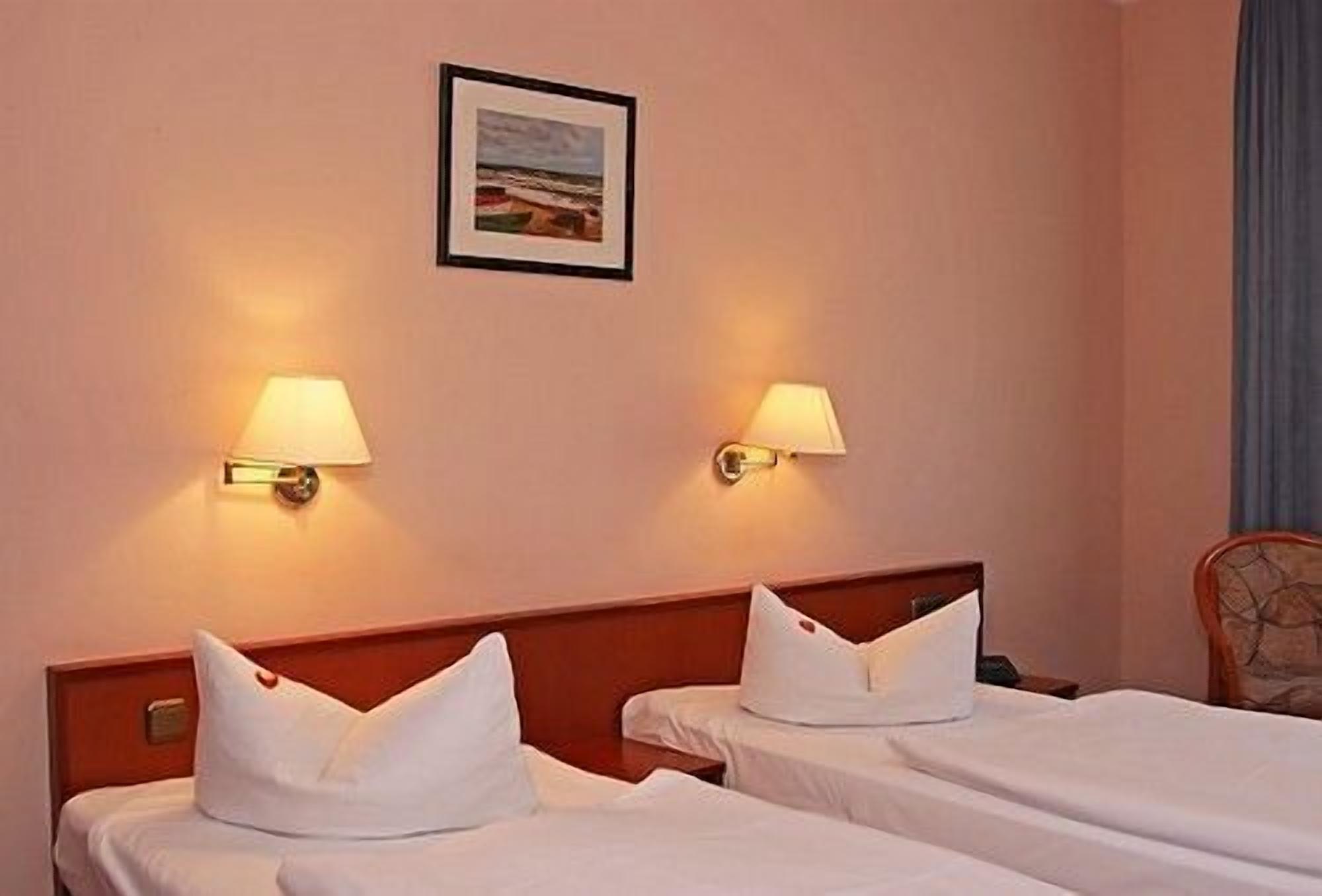 Una habitació d'hotel amb dos llits, cadascun amb roba de llit i almoades blanques, i dues làmpades penjades a la paret.