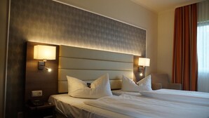 Una habitación de hotel con una cama grande, dos lámparas de noche, una mesita de noche y una silla.
