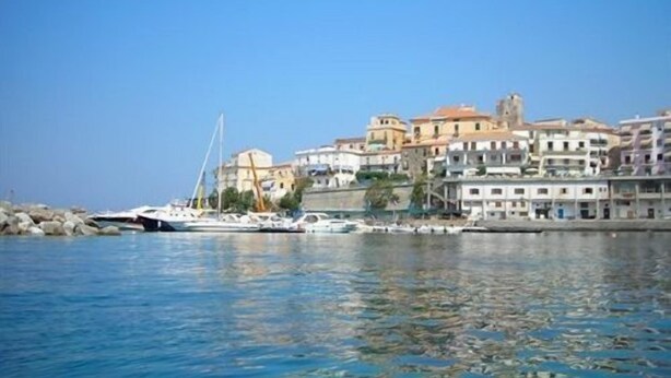 Un pueblo costero con edificios a lo largo del malecón, cielo azul despejado y barcos amarrados cerca de la orilla.