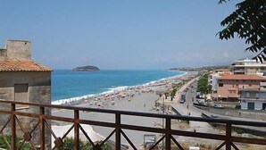 Vista costera con playa, una pequeña isla y edificios a lo largo de la orilla.