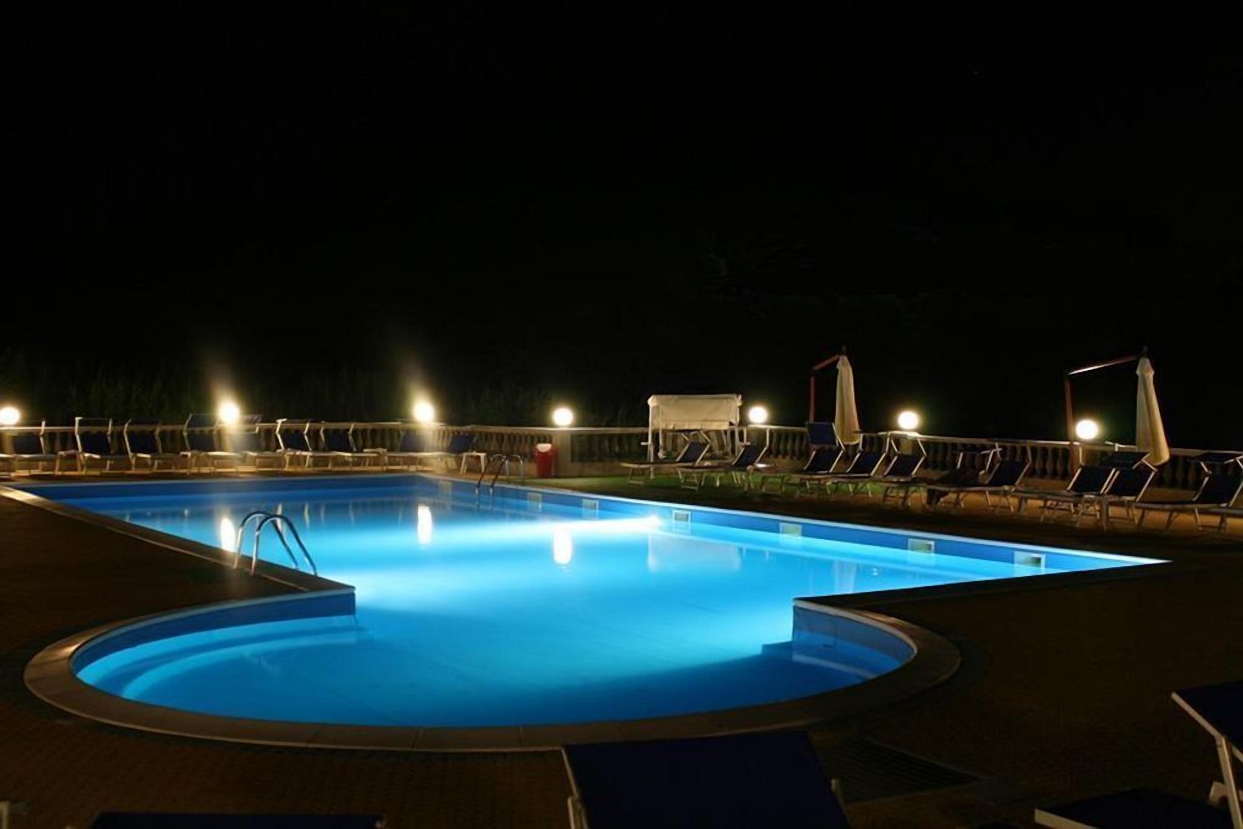 En swimmingpool om natten med liggestole og lys.