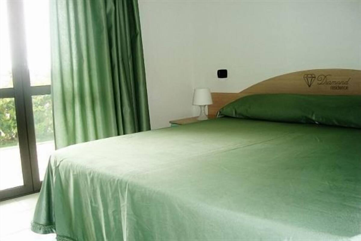 Ein Hotelzimmer mit Bett, Nachttisch, Lampe und einem Fenster mit Vorhängen.
