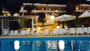 Una piscina con sillas de descanso y sombrillas, rodeada de edificios y árboles.