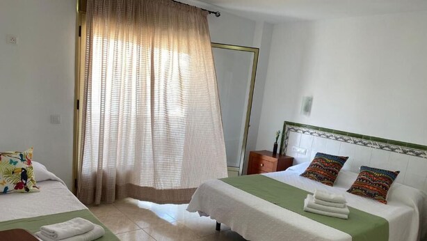 A hotel room with two beds, a large window with curtains, a wooden nightstand, and a green bedspread. - Hotel Matalascañas (Almonte)