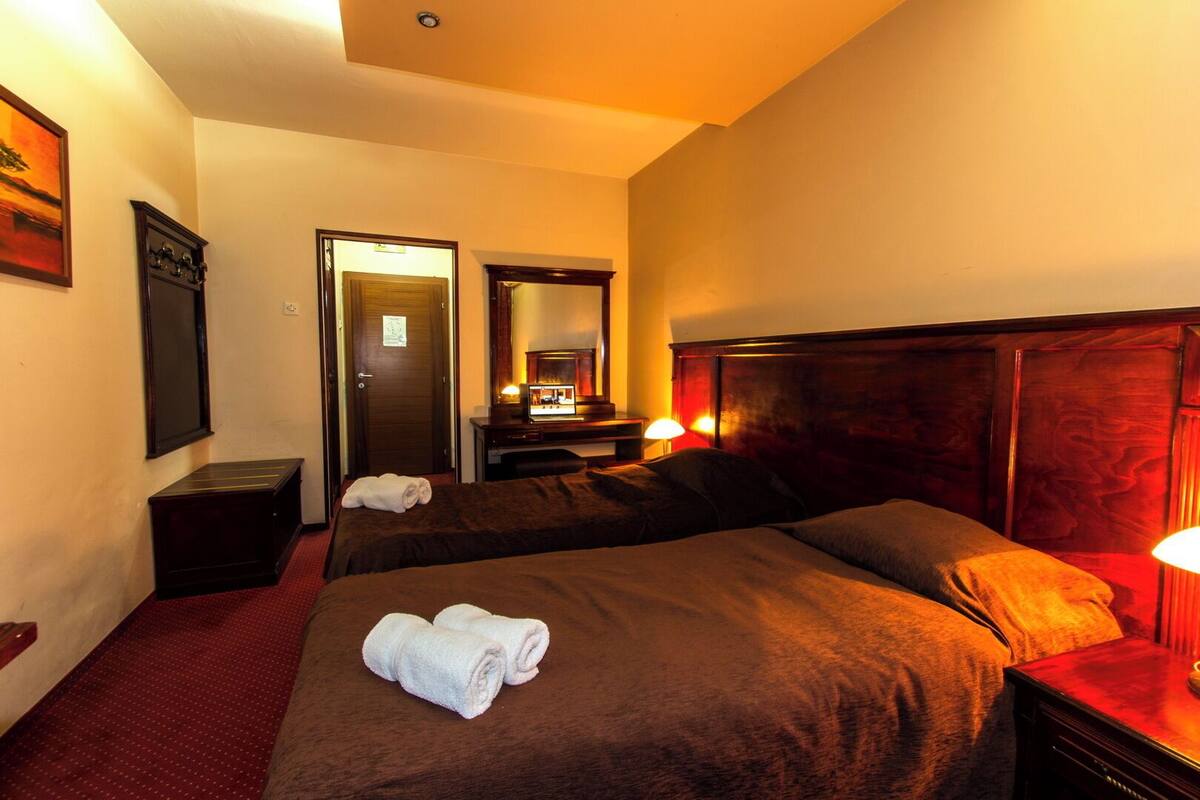 A hotel room with two beds, a desk, a mirror, and a door.