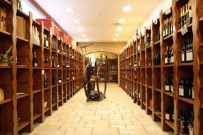 Une cave à vin avec des étagères en bois remplies de bouteilles, une allée centrale et un sol en briques.