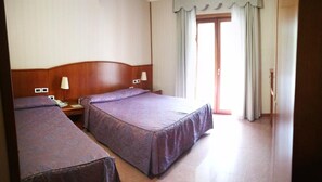 Habitación de hotel con dos camas, cabecero de madera, lámparas de noche, teléfono y una puerta que da a un balcón.