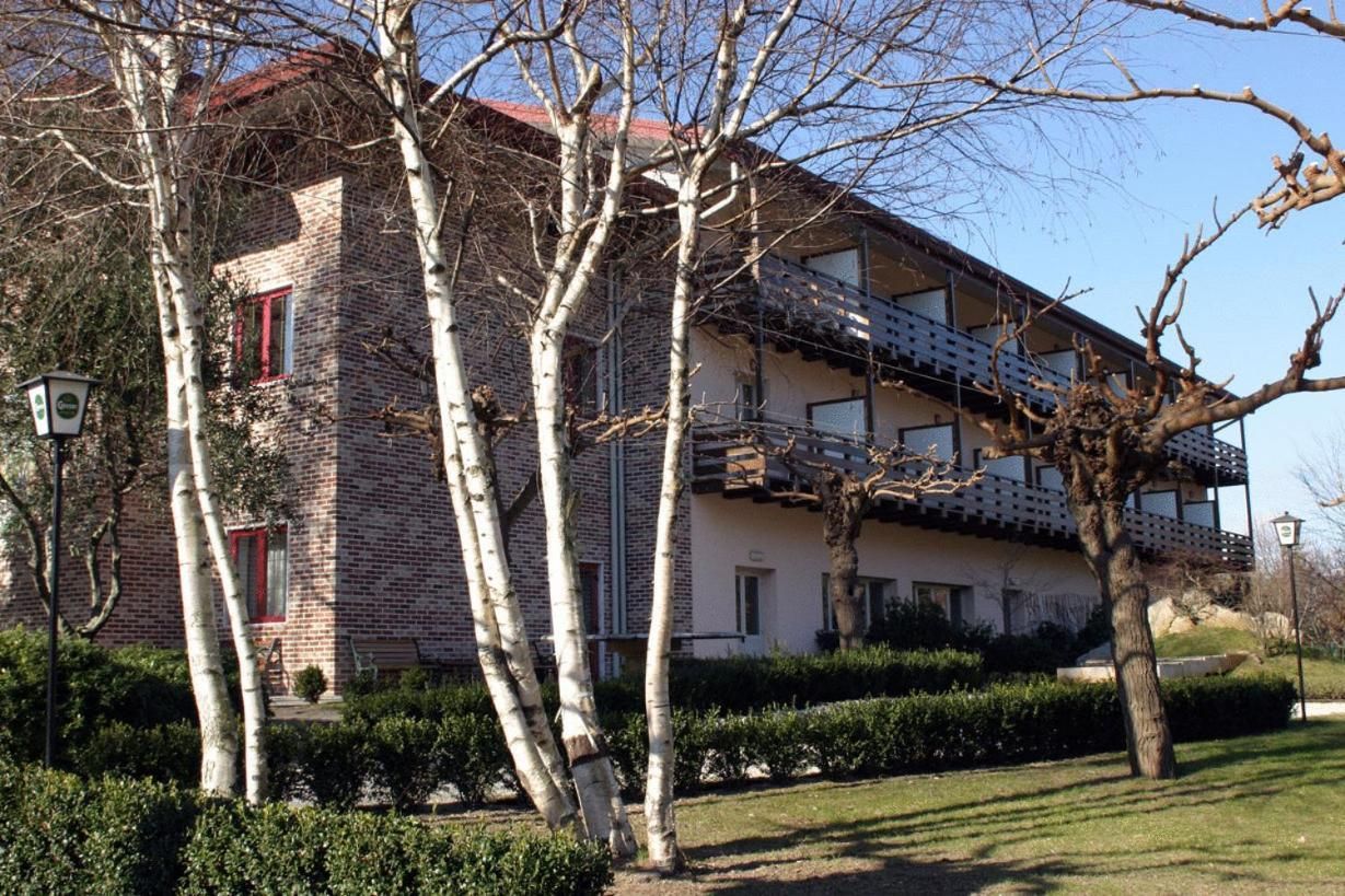 Ein zweistöckiges Gebäude mit Ziegelverkleidung, einem Balkon im oberen Stockwerk und einem Baum im Vordergrund.