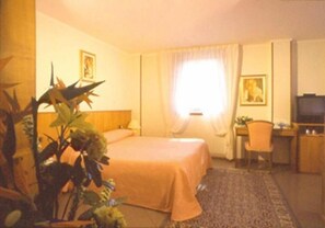 A hotel room with a bed, a desk, a television, and a window with curtains.