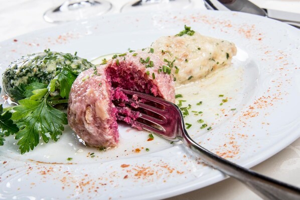 A plate with a meat dish, a dumpling, and a green sauce, garnished with herbs. - Turmhotel Gschwendt (Valle di Casies)