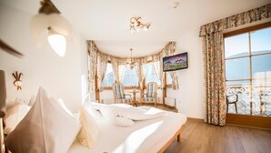 A bedroom with a bed, a desk, two chairs, a television, and a view of the sea. - Turmhotel Gschwendt (Valle di Casies)