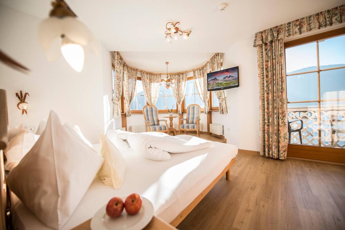 A bedroom with a bed, a desk, two chairs, a television, and a view of the sea.