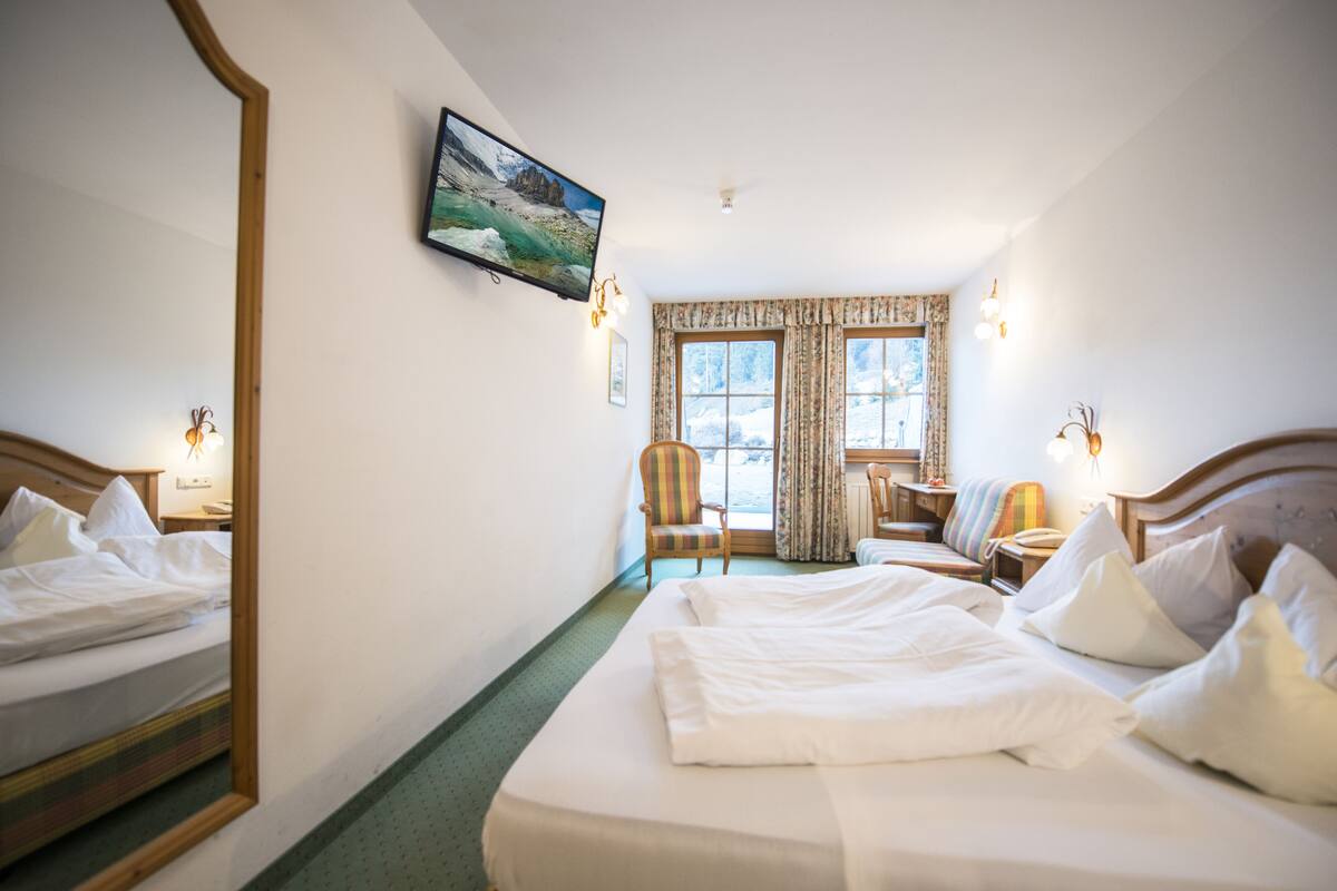 A hotel room with two beds, a television, a chair, a small table, and a window with curtains.