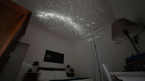 A bedroom with a bed, a nightstand, a lamp, a ceiling projector, and a wall-mounted picture. - Domus Quiritum (Rome)