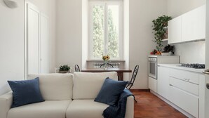A modern kitchen with white cabinets, a dining table with chairs, and a window with a view of trees. - Domus Quiritum (Rome)