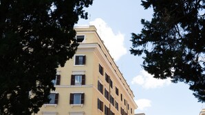 A multi-story building with a yellow facade, multiple windows with shutters, and a clear sky in the background. - Domus Quiritum (Rome)