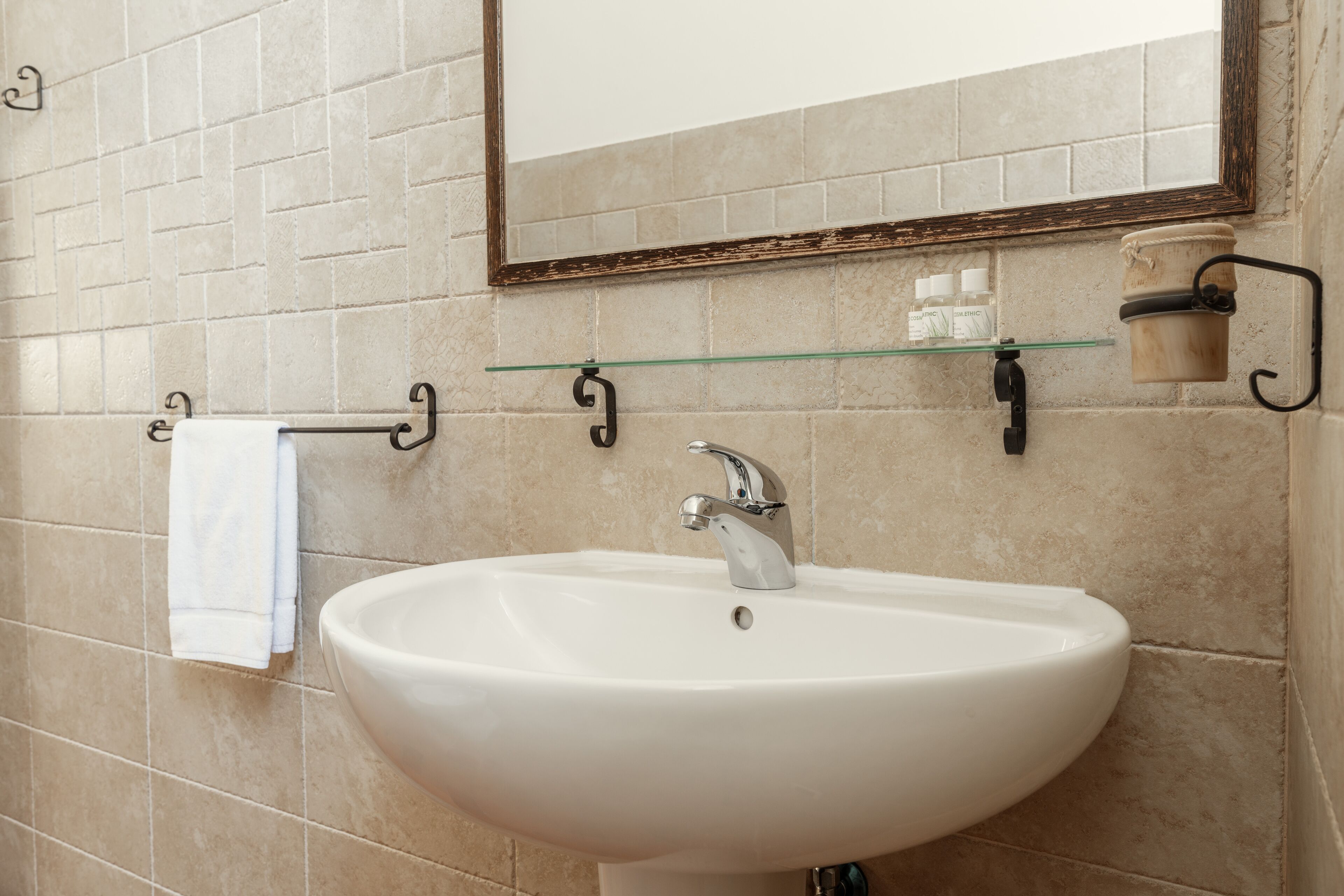 Un baño con lavamanos blanco, espejo y toallero.