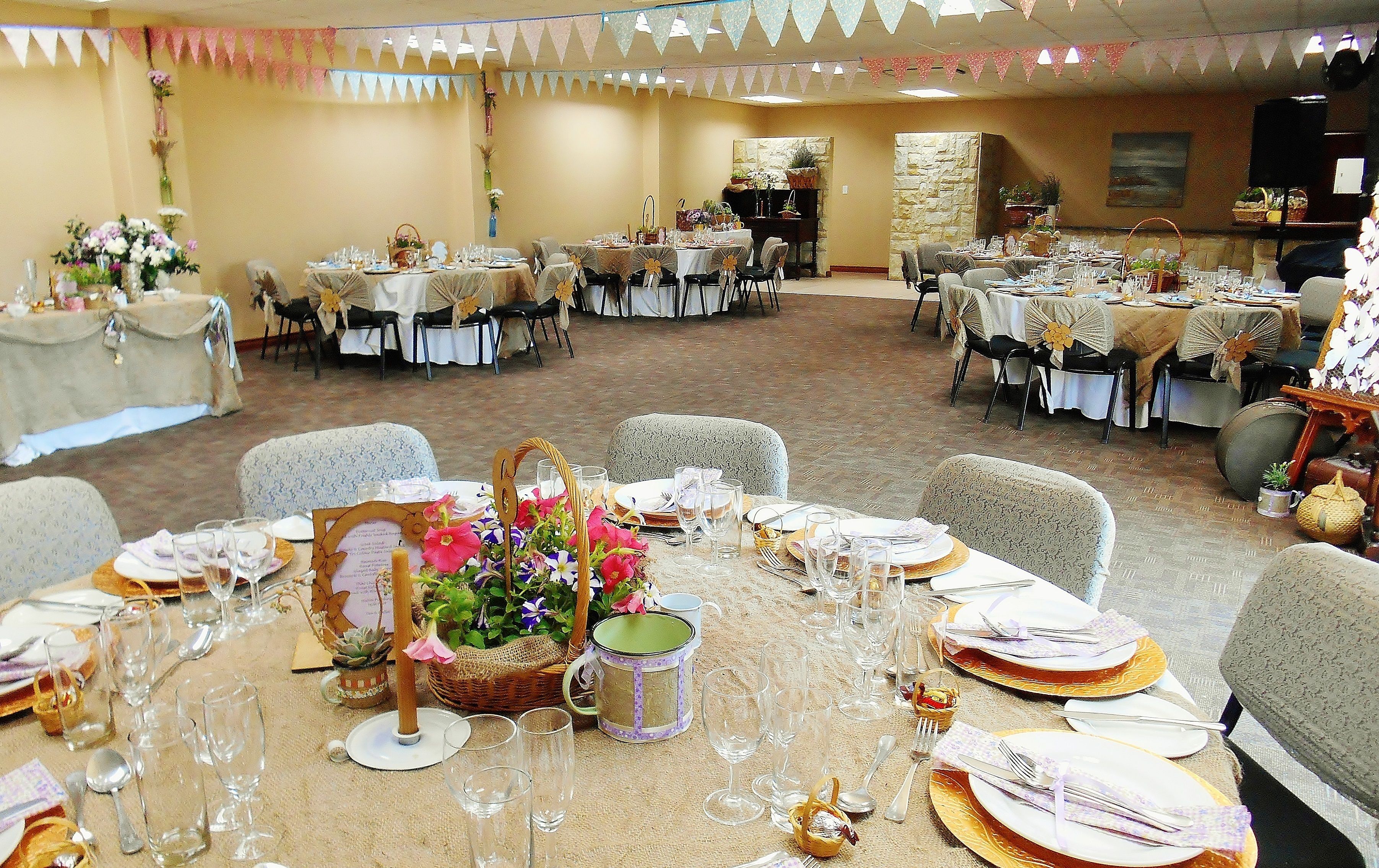 Un salón de banquetes con varias mesas redondas dispuestas para el servicio de comidas, cada una con sillas y vajilla.