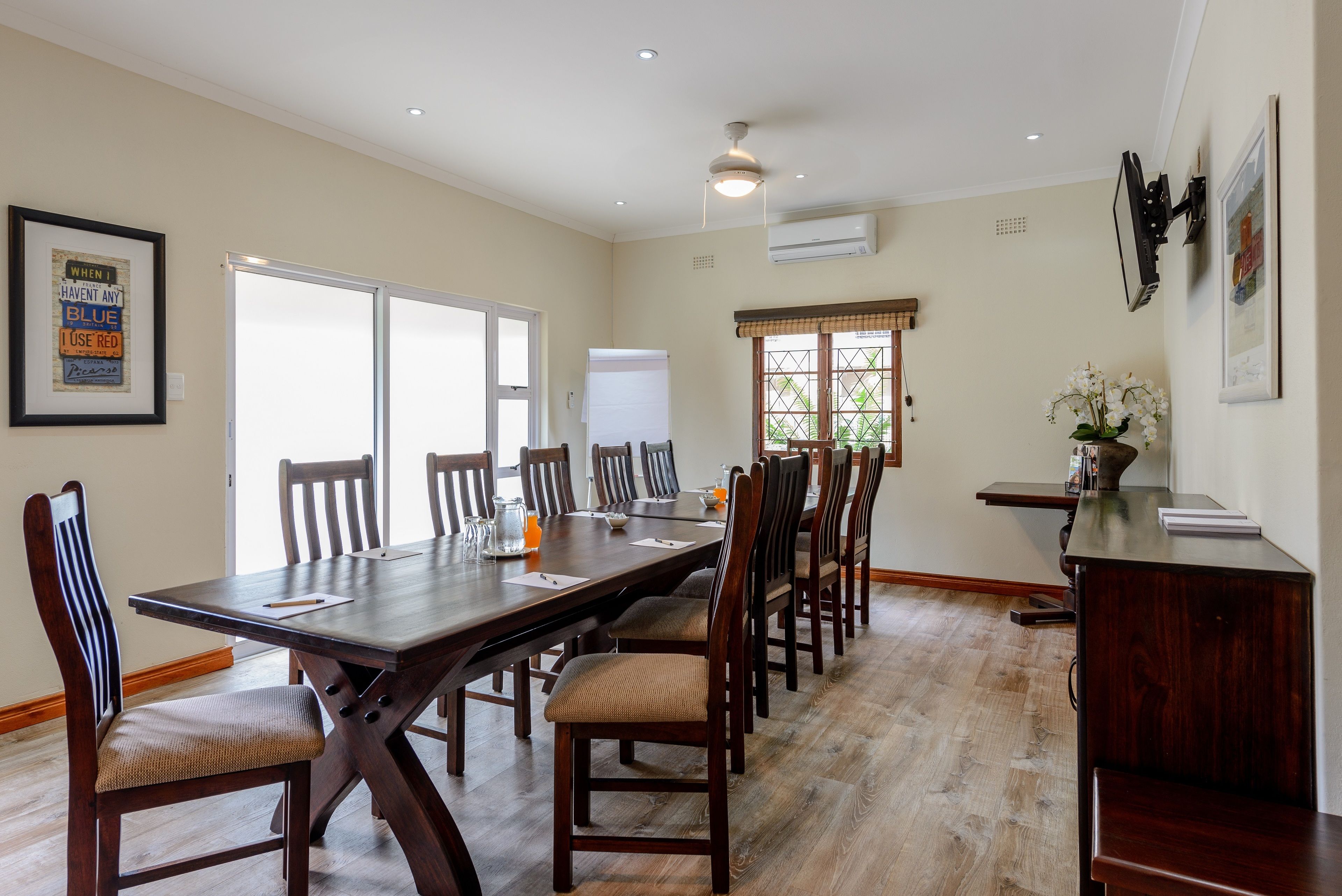 A dining area with a long wooden table, multiple chairs, and a small side table with a vase of flowers.