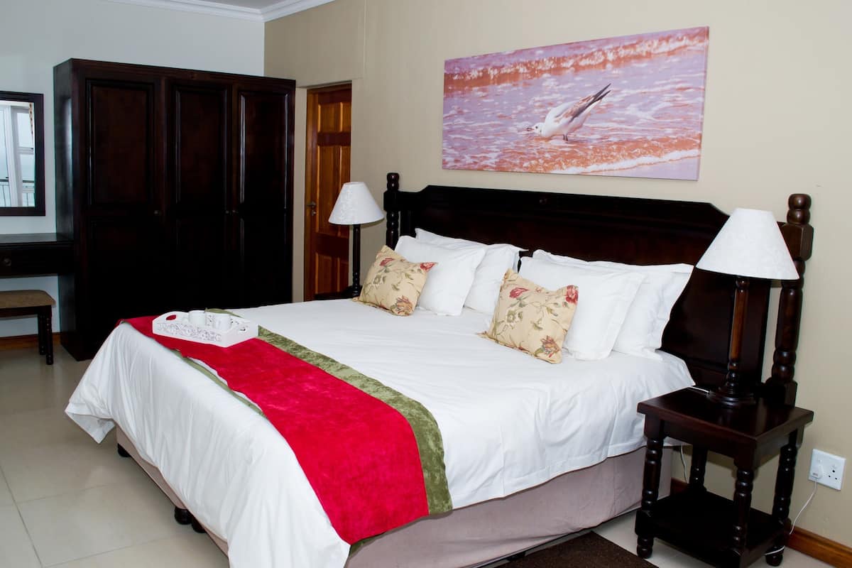 A neatly made bed with a red and green bedspread, a wooden headboard, and two bedside lamps.
