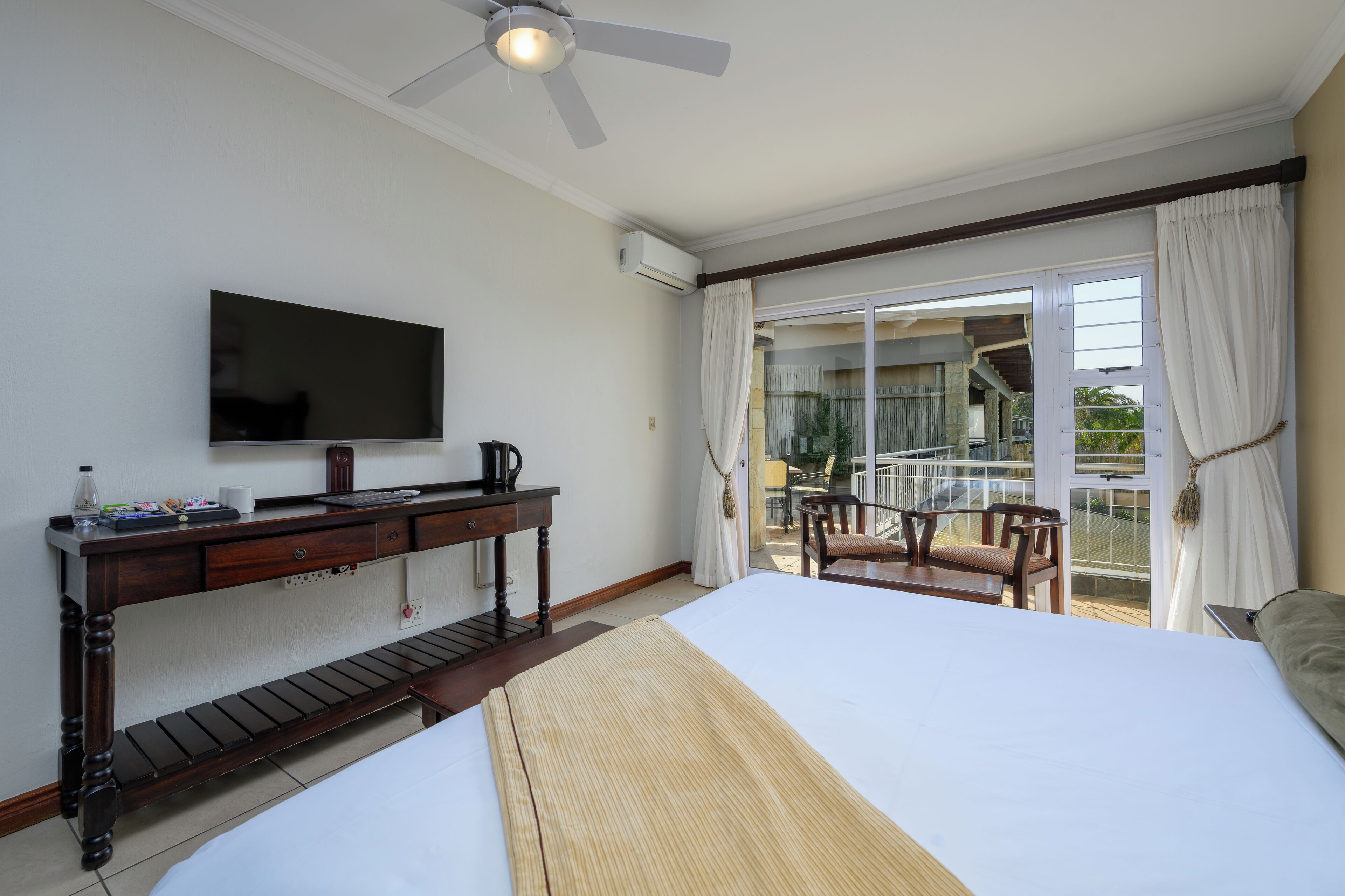 Habitación de hotel con una cama, un escritorio con televisor de pantalla plana, cafetera y vistas al balcón exterior.