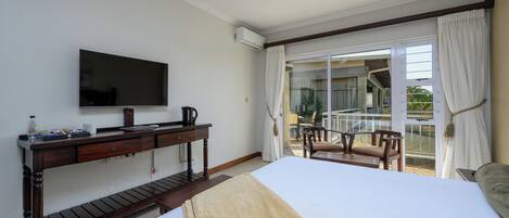 Habitación de hotel con una cama, un escritorio con televisor de pantalla plana, cafetera y vistas al balcón exterior.