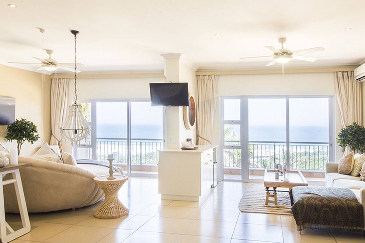 A spacious living room with a balcony, a flat-screen TV, and a ceiling fan.