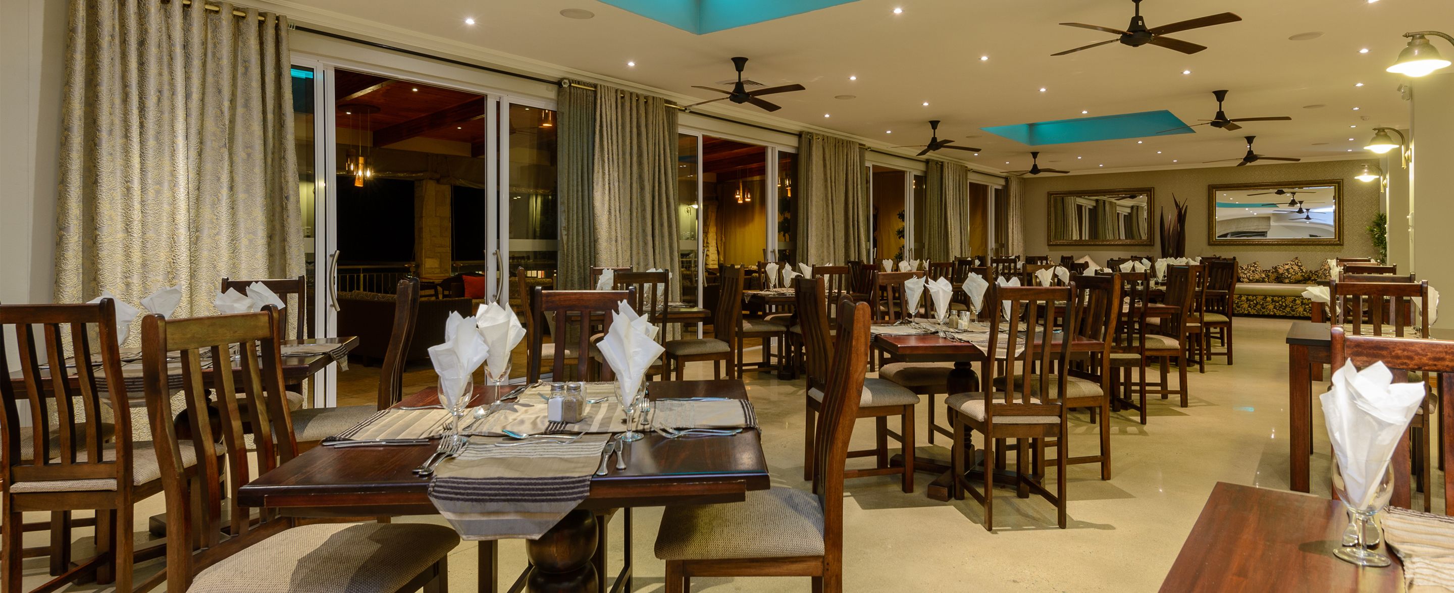 Un restaurante con varias mesas y sillas, ventiladores de techo y un espejo grande en la pared.