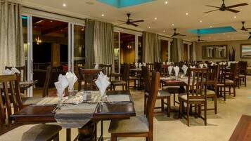 Un restaurante con varias mesas y sillas, ventiladores de techo y un espejo grande en la pared.