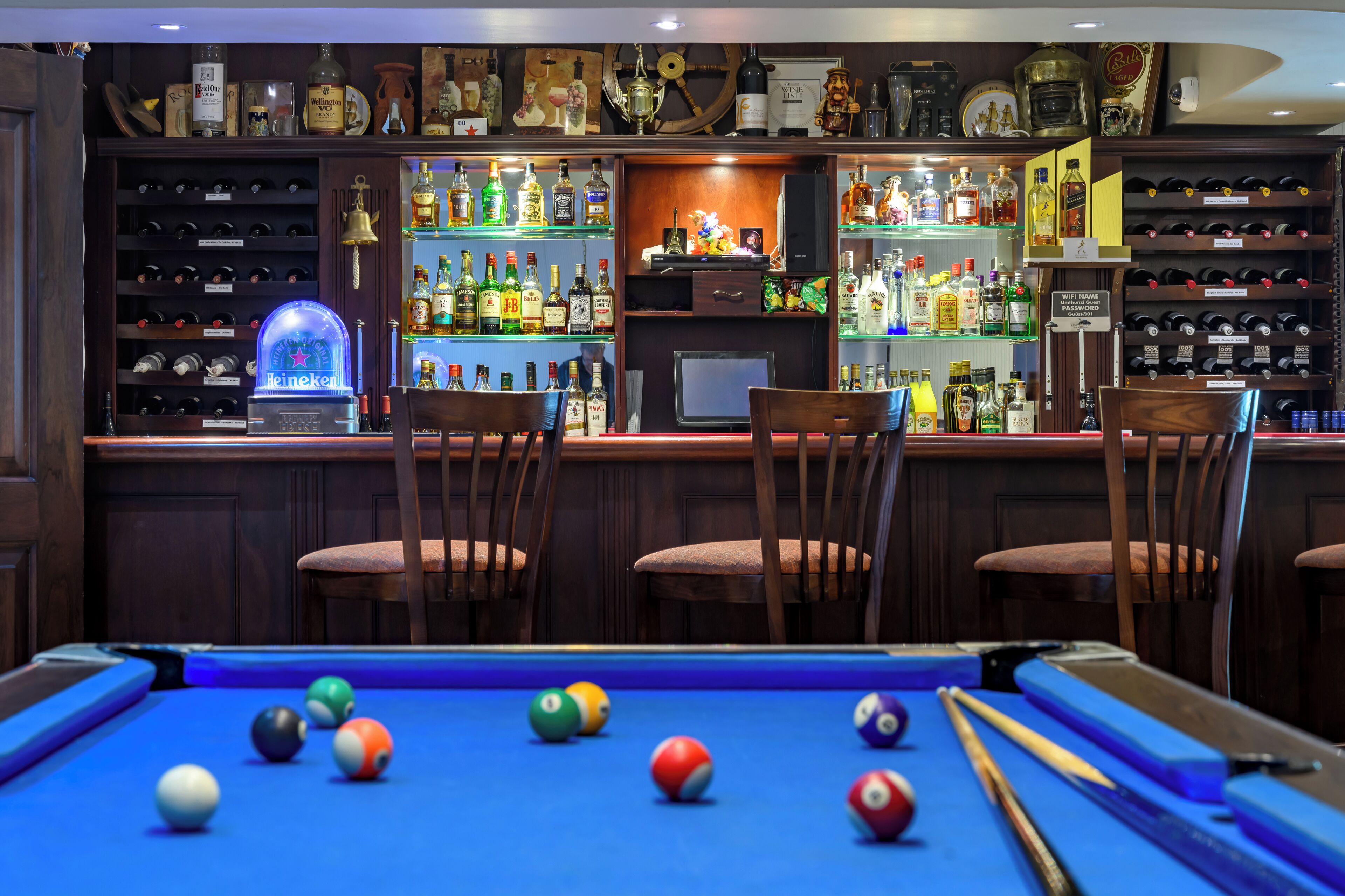Un espace bar équipé d’une table de billard, de chaises et d’étagères remplies de bouteilles d’alcool.