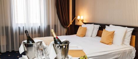 A hotel room with a bed, a nightstand with a bottle of champagne, two glasses, and a fruit platter.