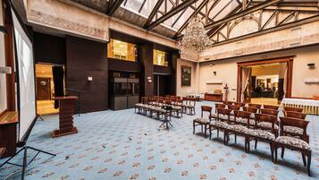 A spacious hall with a high ceiling and a chandelier, arranged seating, and a stage with a podium.
