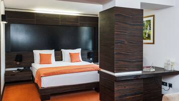 A modern hotel room with a large bed, dark wood headboard, and a desk with a lamp.