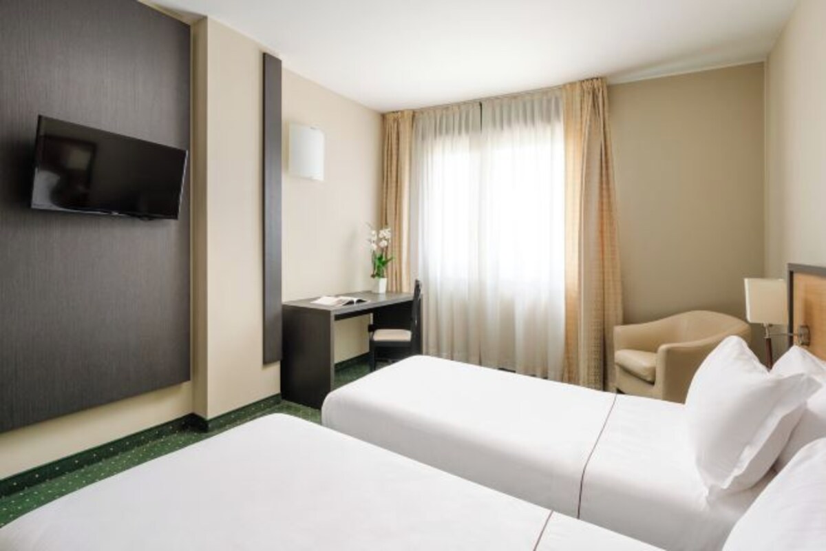 A hotel room with two beds, a desk, a chair, a TV, and a window with curtains.