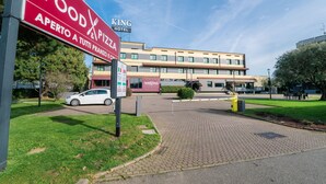 A hotel with a sign for a food and pizza restaurant, a paved entrance, and a car parked nearby. - Smart Hotel King , by R Collection Hotels (Varedo)