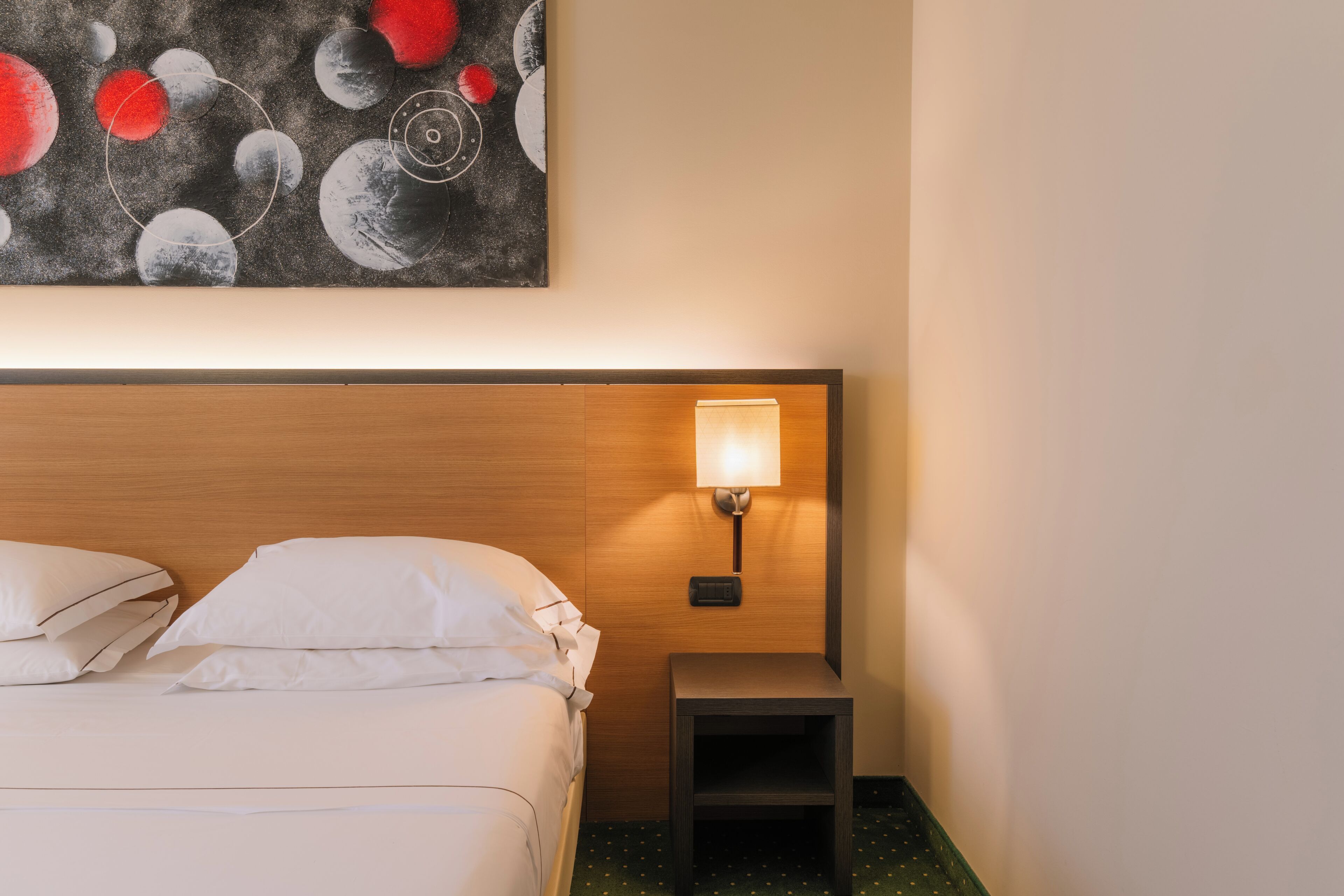 Habitación de hotel con cama, mesita de noche, lámpara de pared y un cuadro de cuerpos celestes.