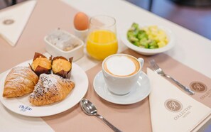A breakfast setting with croissants, a cup of coffee, a glass of orange juice, a bowl of salad, and a plate with an egg.