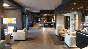 A modern hotel lobby with a reception desk, seating area, and a bar.