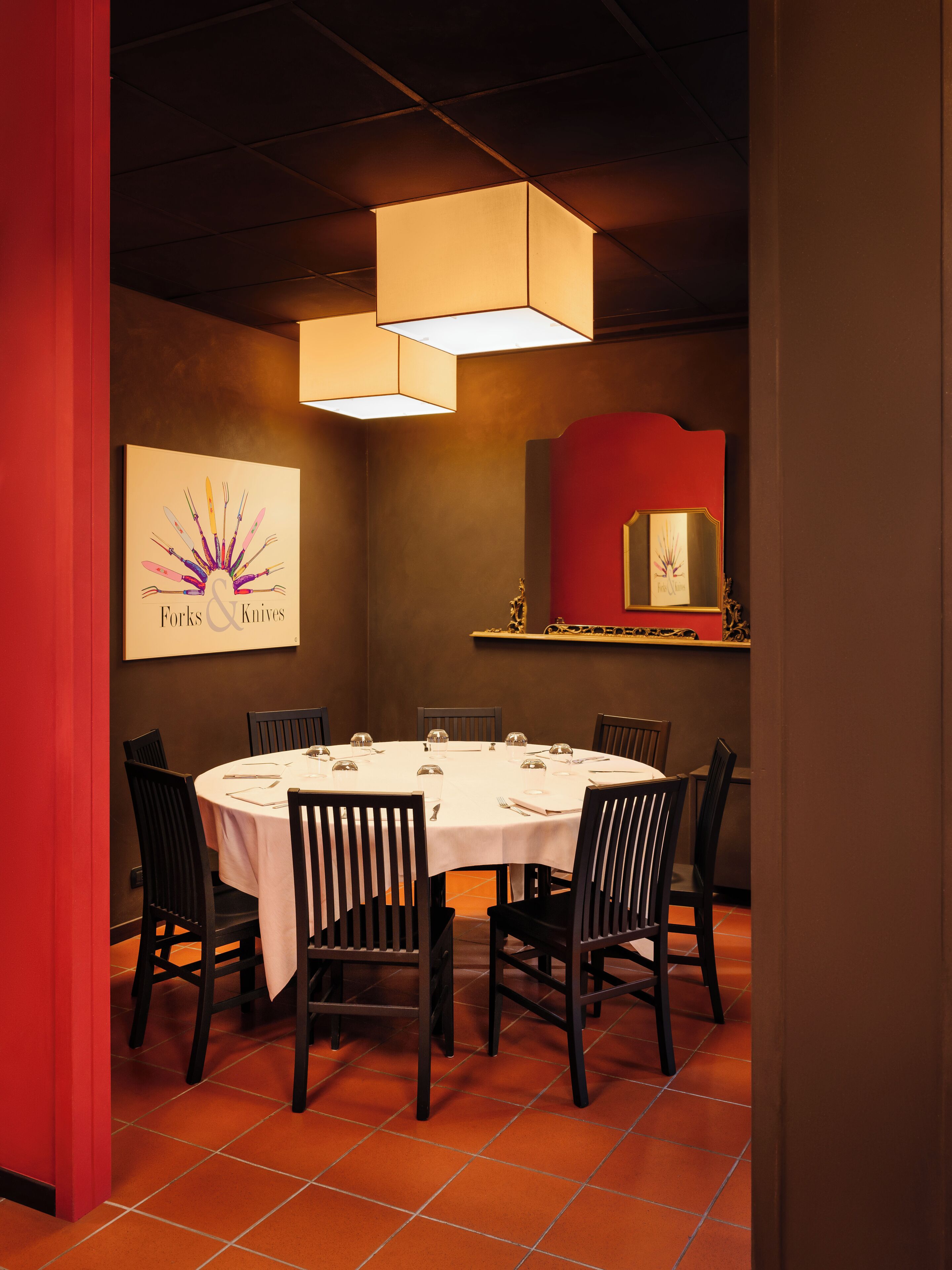 A dining area with a round table, six chairs, and a white tablecloth. There is a wall-mounted clock and a framed artwork above the table.