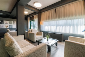 A modern lounge area with patterned sofas, a coffee table, and a large window with curtains. - Smart Hotel King , by R Collection Hotels (Varedo)