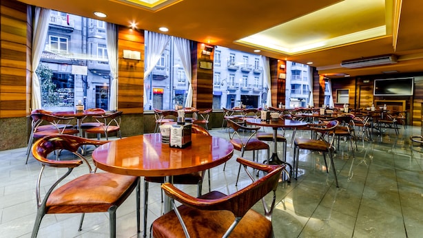A spacious restaurant with multiple round tables and chairs, large windows with curtains, and a modern interior design.