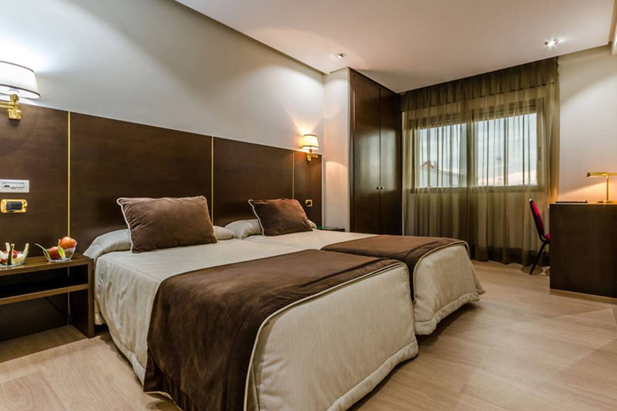 A modern hotel room with a large bed, bedside tables, a desk, and a window with curtains.